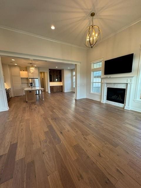 unfurnished living room with a high end fireplace, crown molding, recessed lighting, an inviting chandelier, and dark wood-style flooring