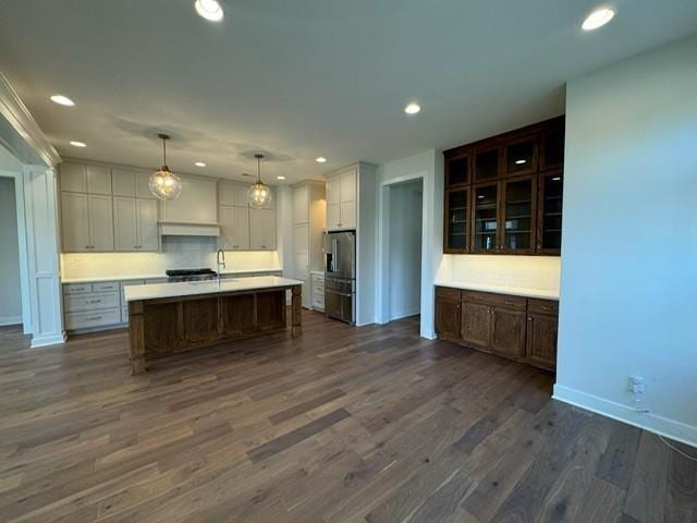 kitchen featuring a center island with sink, recessed lighting, stainless steel fridge, light countertops, and dark wood-style flooring