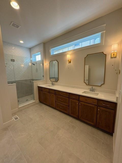 full bath featuring double vanity, visible vents, a stall shower, and a sink