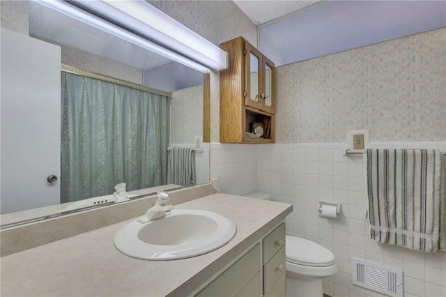 full bathroom with visible vents, wallpapered walls, wainscoting, tile walls, and toilet