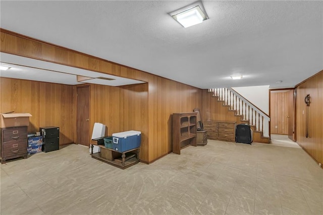 finished below grade area featuring wooden walls, light floors, a textured ceiling, and stairs