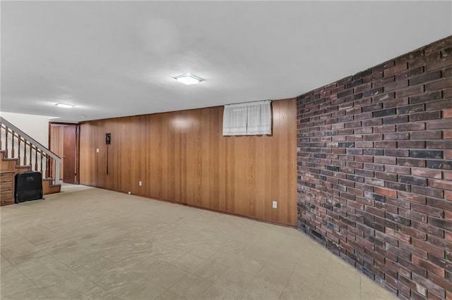 finished below grade area featuring stairway, light floors, brick wall, and wooden walls