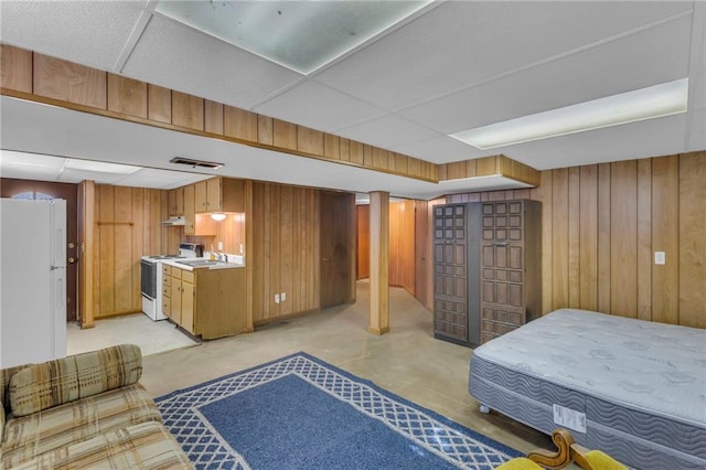 bedroom featuring visible vents, freestanding refrigerator, a sink, a paneled ceiling, and wood walls