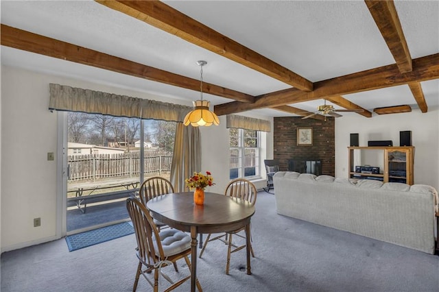 dining space with ceiling fan, beamed ceiling, carpet flooring, a fireplace, and a textured ceiling