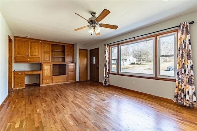 unfurnished living room with ceiling fan, light wood-style flooring, and built in study area