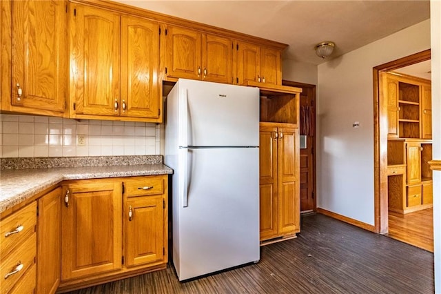 kitchen with backsplash, dark wood finished floors, freestanding refrigerator, brown cabinetry, and baseboards