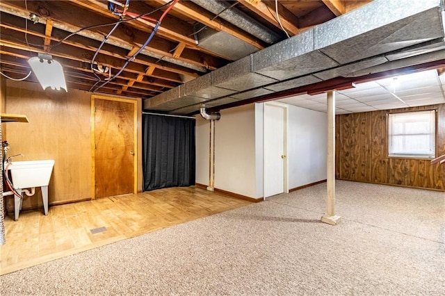 basement featuring wooden walls, carpet flooring, a drop ceiling, and a sink