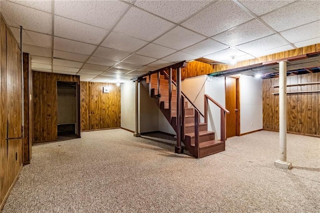 finished basement with a drop ceiling, wood walls, stairs, and carpet floors