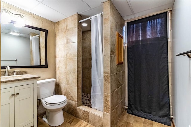 bathroom featuring a shower stall, toilet, vanity, wood finished floors, and tile walls