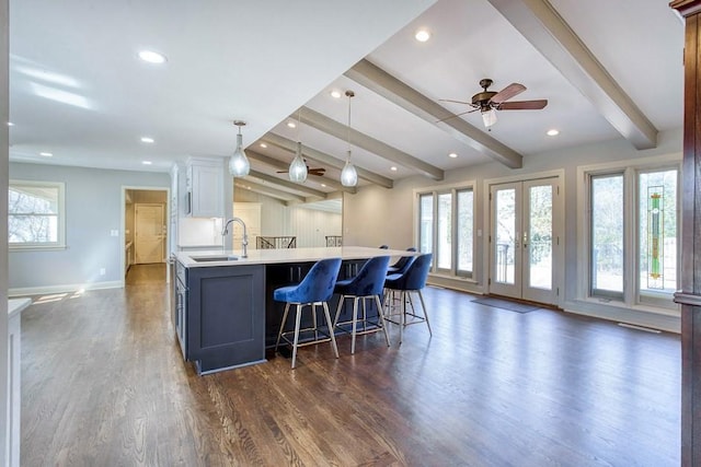 kitchen with beamed ceiling, a sink, plenty of natural light, light countertops, and dark wood-style flooring