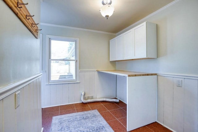 clothes washing area featuring a wainscoted wall, laundry area, crown molding, and dark tile patterned flooring