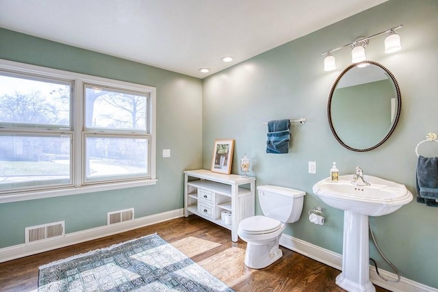 half bath with visible vents, toilet, baseboards, and wood finished floors