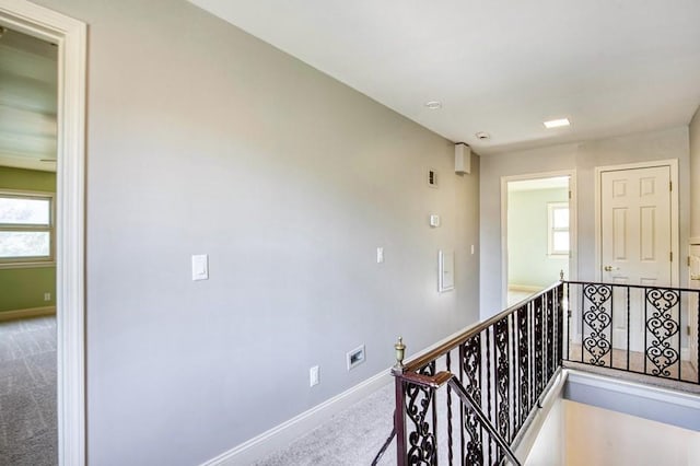 hallway featuring baseboards, an upstairs landing, and carpet