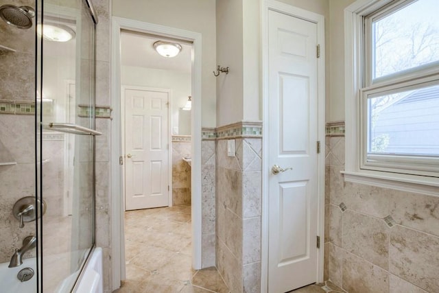 bathroom featuring a wainscoted wall, tile walls, plenty of natural light, and combined bath / shower with glass door