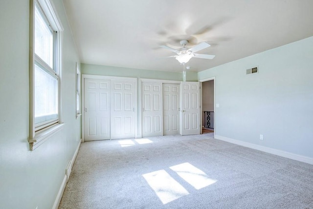 unfurnished bedroom with carpet flooring, baseboards, visible vents, and two closets