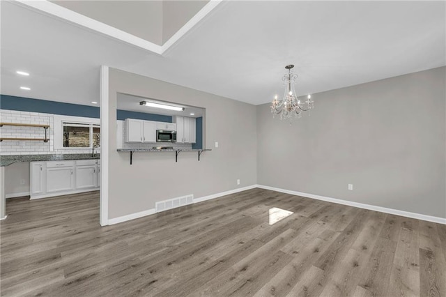 unfurnished living room featuring visible vents, a notable chandelier, light wood-style flooring, recessed lighting, and baseboards