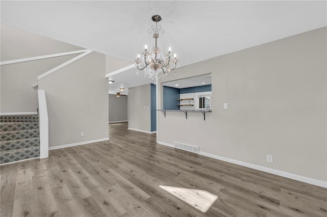 unfurnished living room with visible vents, ceiling fan with notable chandelier, baseboards, and wood finished floors