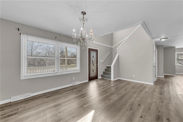 unfurnished living room with visible vents, an inviting chandelier, wood finished floors, and stairway