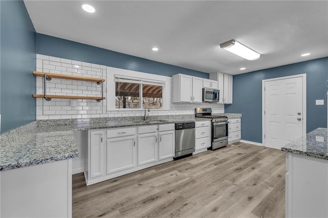 kitchen with light stone countertops, light wood-style flooring, a sink, appliances with stainless steel finishes, and white cabinetry