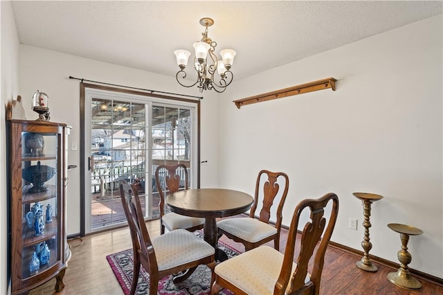 dining area with baseboards, a textured ceiling, an inviting chandelier, and wood finished floors