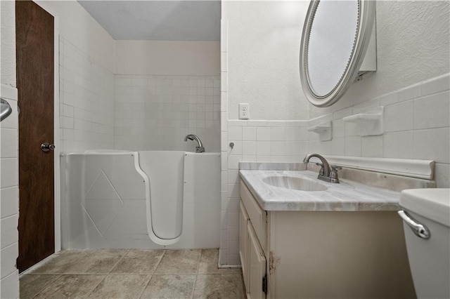 bathroom featuring tile walls, a bath, vanity, and a textured wall