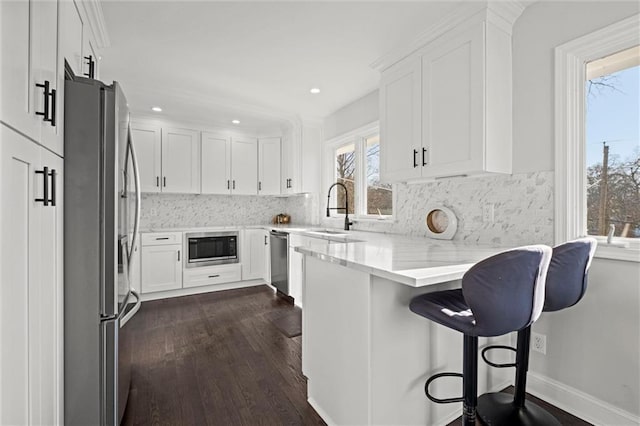 kitchen with white cabinetry, a peninsula, stainless steel appliances, and a sink