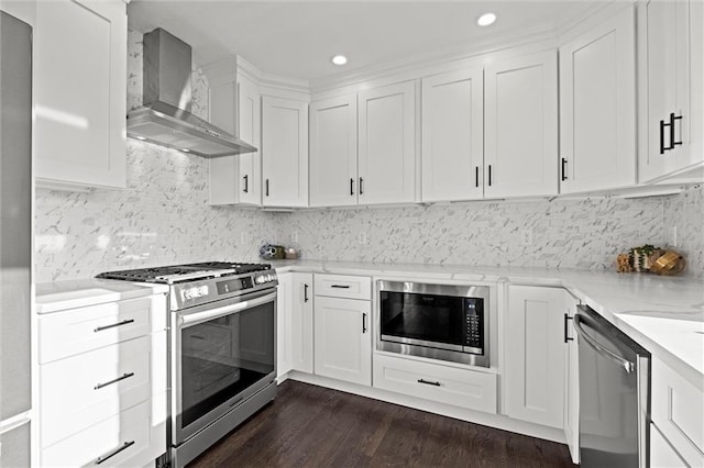 kitchen with light stone counters, dark wood-style flooring, white cabinets, appliances with stainless steel finishes, and wall chimney exhaust hood