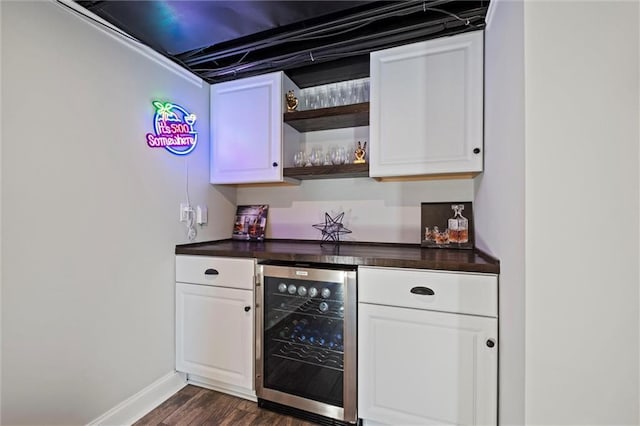 bar with a bar, beverage cooler, dark wood-style flooring, and baseboards