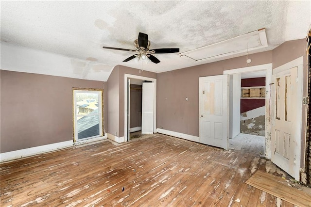 unfurnished bedroom with a textured ceiling, attic access, baseboards, and hardwood / wood-style floors