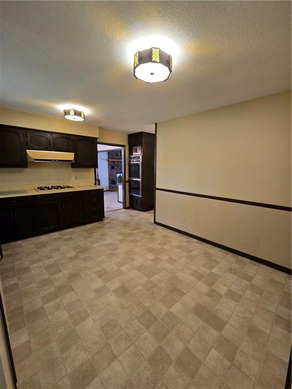 2213 Millwood Dr, Atchison, KS 66002 - kitchen with under cabinet range hood, light countertops, a textured ceiling, light floors, and white gas stovetop