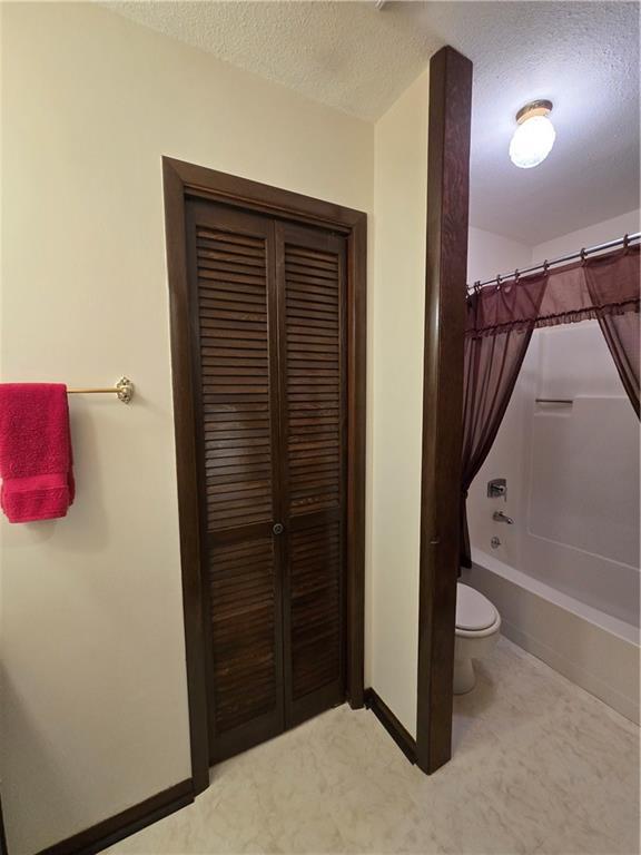 2213 Millwood Dr, Atchison, KS 66002 - bathroom featuring a textured ceiling, shower / bathtub combination with curtain, and a closet