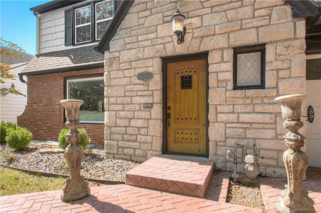 entrance to property with stone siding and a shingled roof