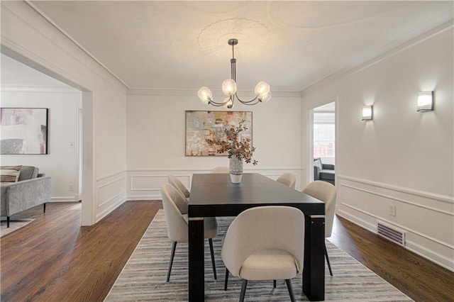 dining area featuring visible vents, dark wood-type flooring, wainscoting, crown molding, and a notable chandelier