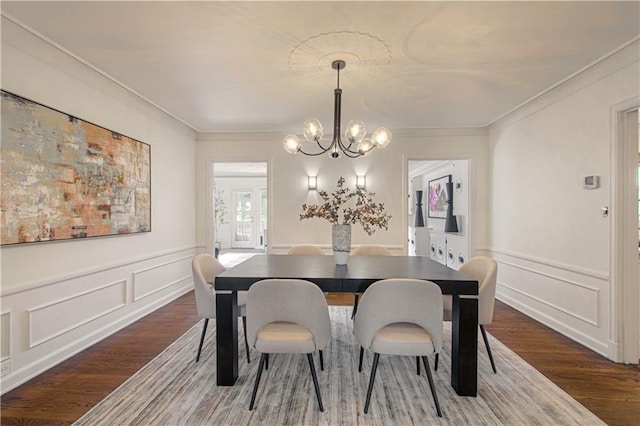 dining space featuring an inviting chandelier, a decorative wall, wood finished floors, and ornamental molding