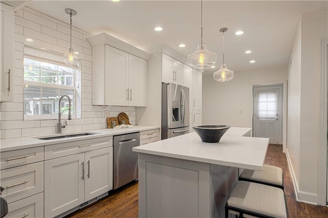 kitchen with a sink, a kitchen island, appliances with stainless steel finishes, white cabinets, and decorative backsplash