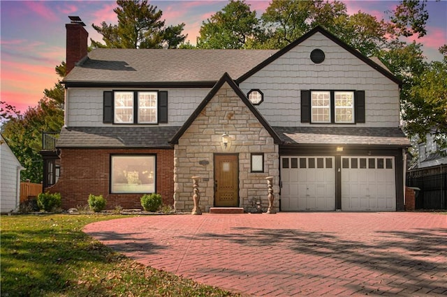 view of front of house featuring an attached garage, a shingled roof, a chimney, stone siding, and decorative driveway