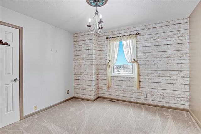 empty room with baseboards, a chandelier, wood walls, carpet floors, and a textured ceiling