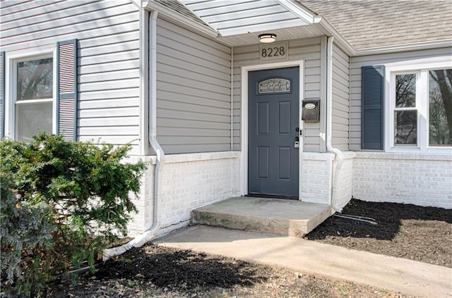 view of exterior entry with brick siding and roof with shingles