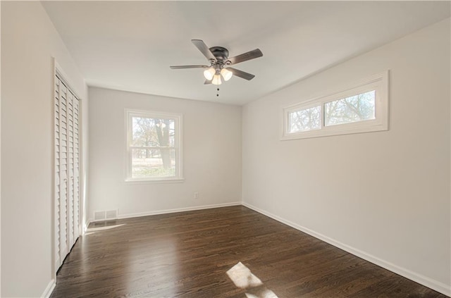 unfurnished bedroom featuring dark wood-style floors, visible vents, multiple windows, and baseboards