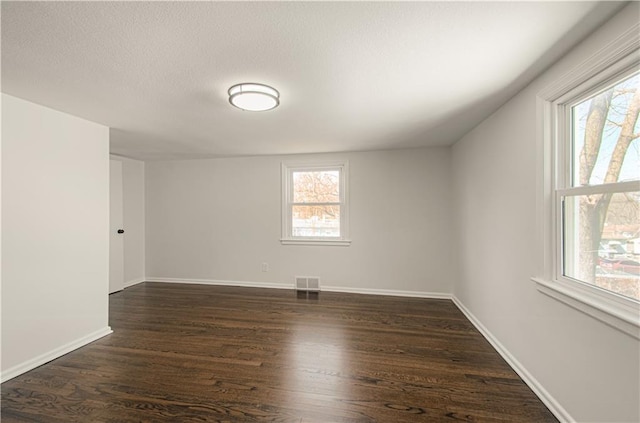 unfurnished room featuring dark wood-style floors, visible vents, a textured ceiling, and baseboards