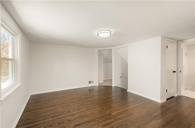 spare room featuring visible vents, dark wood-style flooring, a wealth of natural light, and baseboards