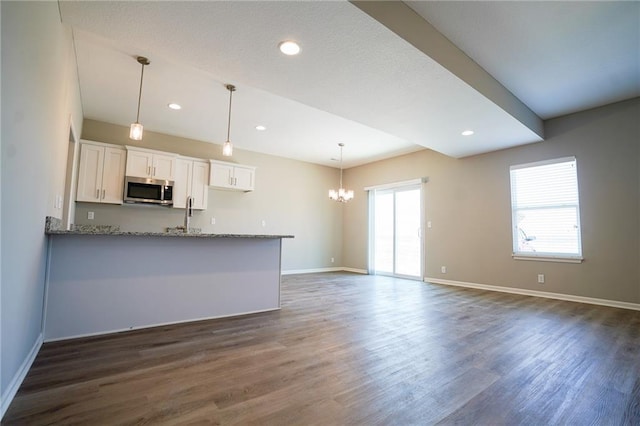 kitchen featuring light stone counters, dark wood-style floors, white cabinetry, stainless steel microwave, and a chandelier