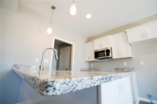 kitchen with light stone countertops, recessed lighting, hanging light fixtures, white cabinetry, and stainless steel microwave