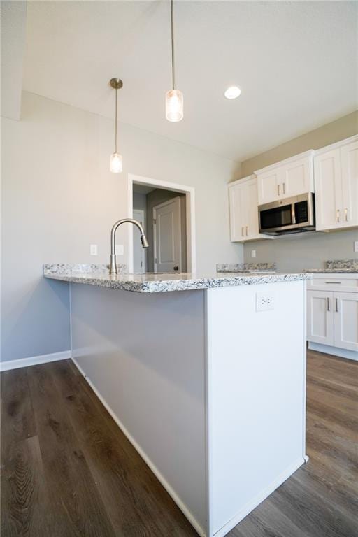 kitchen with light stone counters, stainless steel microwave, white cabinets, and dark wood-style flooring