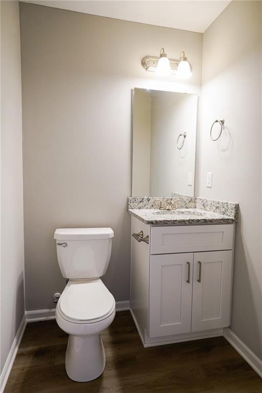 half bath with toilet, vanity, baseboards, and wood finished floors