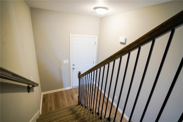 staircase with wood finished floors, baseboards, and a textured ceiling