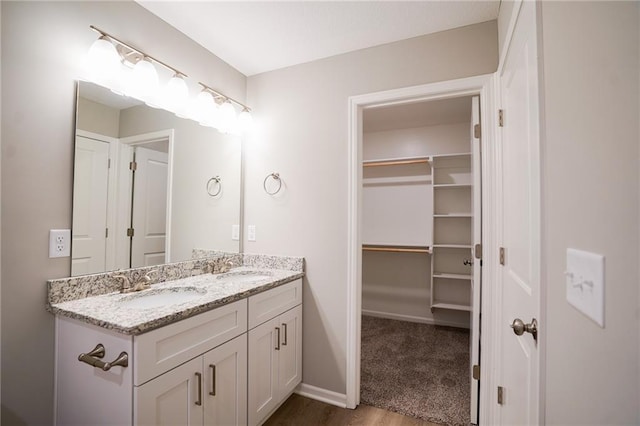 full bath with a spacious closet, a sink, baseboards, and double vanity