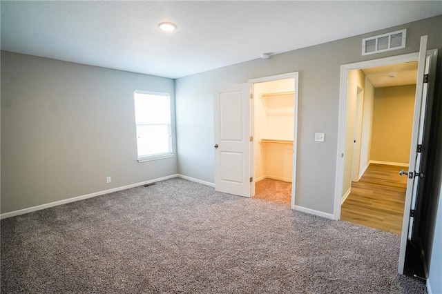 unfurnished bedroom with a walk in closet, carpet flooring, baseboards, and visible vents