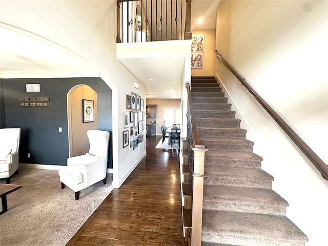 stairs with arched walkways, a high ceiling, baseboards, and wood finished floors