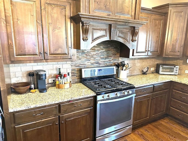 kitchen with light stone countertops, dark wood-style floors, premium range hood, stainless steel gas range, and backsplash